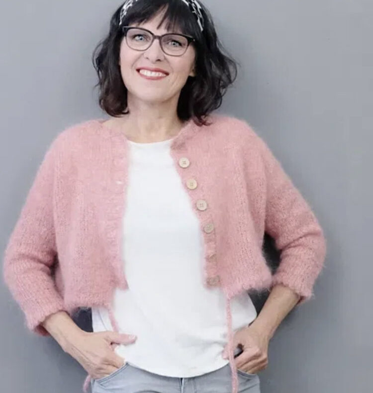 rosa p. Yooko Cardigan – kurzer, kastig geschnittener Strickcardigan mit Raglanärmeln und Mausezähnchenkante, gestrickt in zartrosa Sandnes KOS, getragen über einem weißen Shirt.