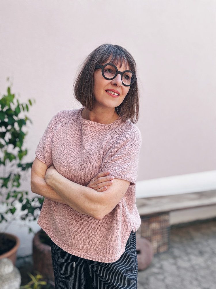 Eezra Shirt Strickanleitung – locker geschnittenes Top-Down-Raglanshirt in zartem Rosa, getragen mit rundem Ausschnitt, kurzen Ärmeln und Boxy-Form mit abgerundetem Saum