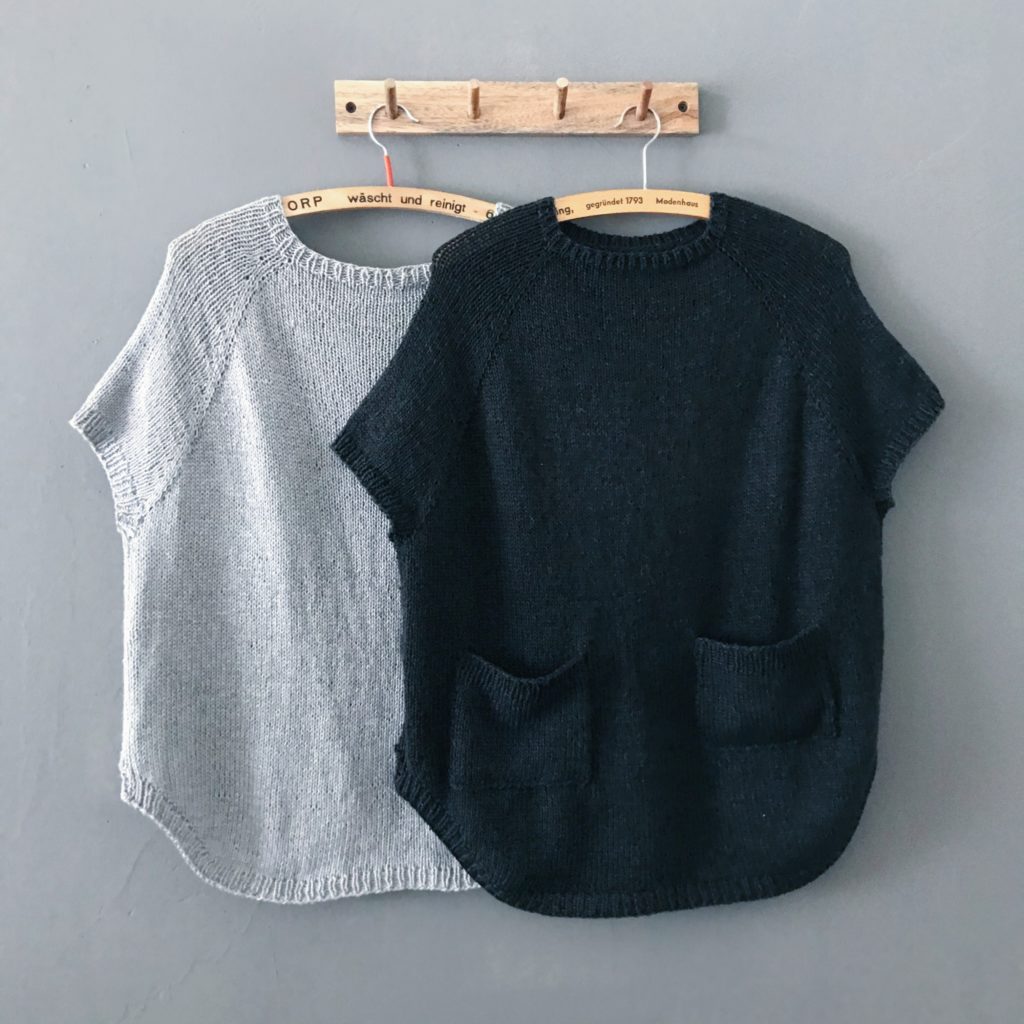 Eezra Shirt, einmal in Grau , einmal in Schwarz, auf Bügeln hängend vor einer grauen Wand