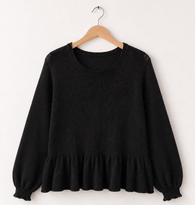 Kate’s Longsleeve in Schwarz als Produktfoto vor einer weißen Wand. Das nahtlos von oben gestrickte Longsleeve zeigt eine schlichte Raglankonstruktion, lange Ballonärmel mit schmalen Bündchen und ein sanft ausgestelltes Rüschenbündchen am Saum.