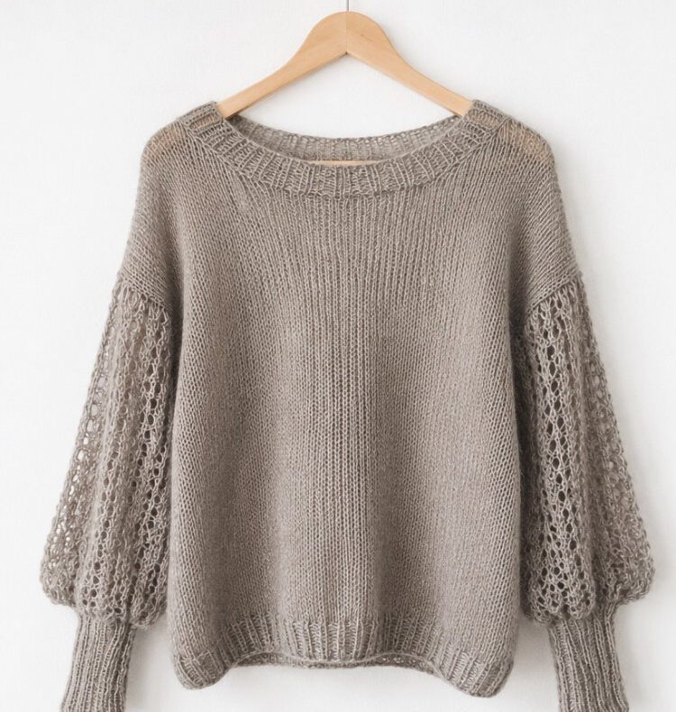 Helle Vreeni Blouse mit langen Lochmusterärmeln auf einem Holzbügel an weißer Wand.