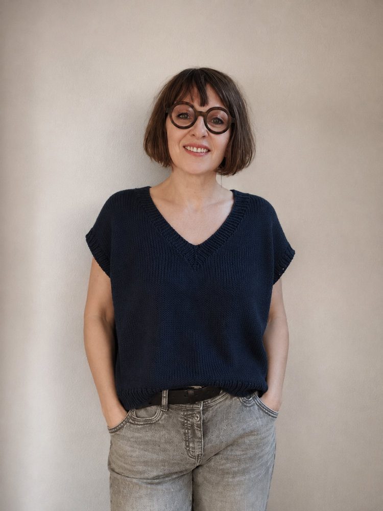 Frau trägt das dunkelblaue Vaahta Tee mit V-Ausschnitt und angeschnittenen Ärmeln zu einer hellgrauen Jeans vor neutralem Hintergrund