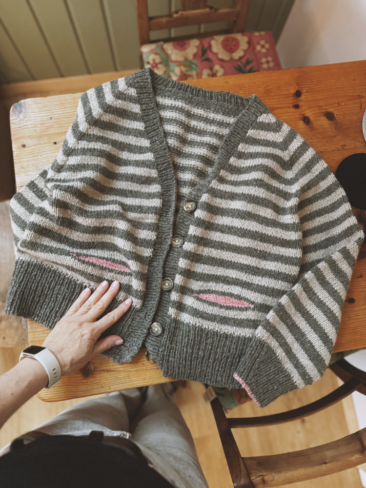 Detailansicht Luumi Cardigan: V-Ausschnitt, angestrickte Knopfblende und breite Rippenbündchen