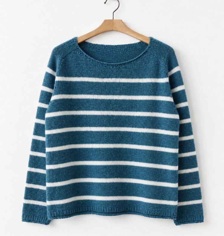 Aarven Longsleeve mit Sattelschulter in Petrol und Weiß, gestreift gestrickt und auf einem Holzbügel vor einer weißen Wand.