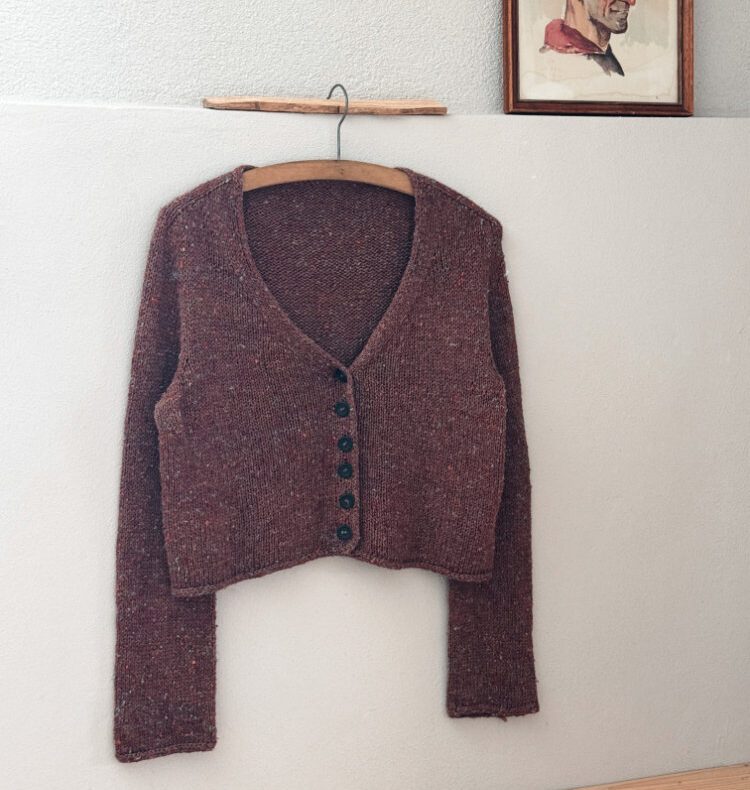 Uukii Cardigan aus BC Garn Tussah Tweed in Braun auf Holzbügel vor heller Wand.