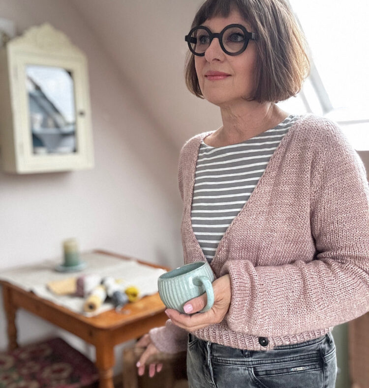 Frau mit Maiija Crossover Cardigan in Rosa und Kaffeetasse am Fenster