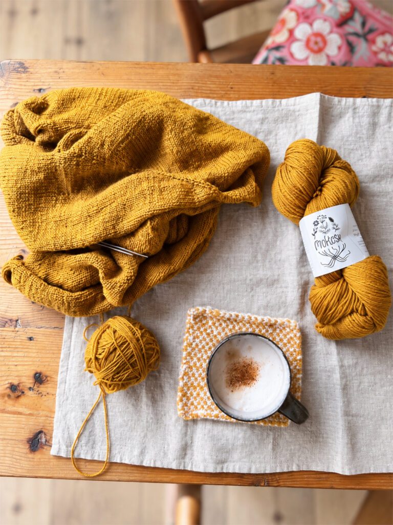 Senfgelbes Strickprojekt mit Garnstrang und gewickeltem Knäuel auf einem Holztisch.