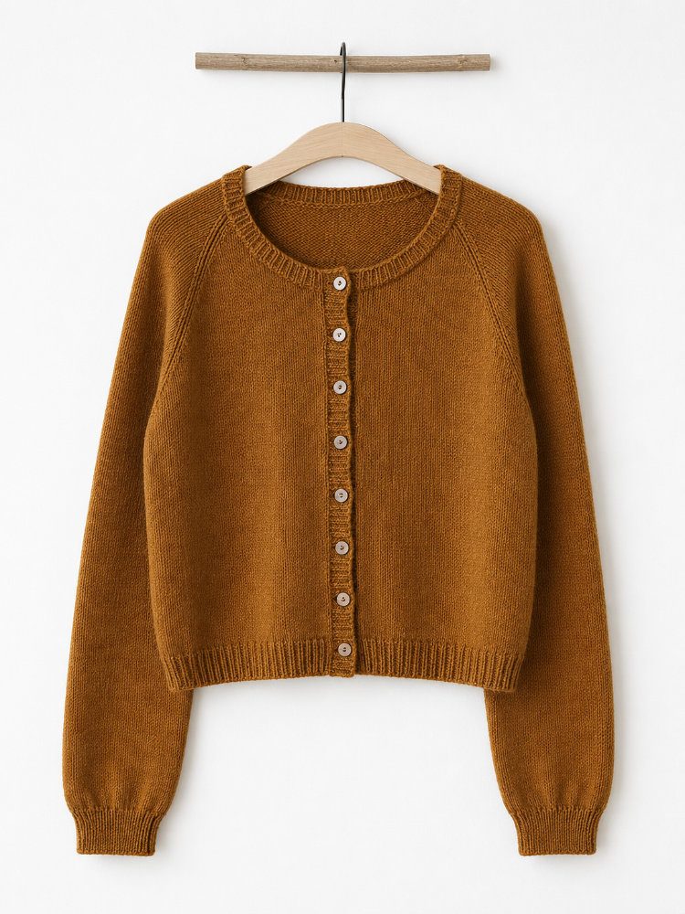 Doorli Cardigan in warmem Ockerton, handgestrickt mit schmaler Raglanlinie, Knopfleiste und langen Ärmeln, auf Holzbügel vor weißer Wand.