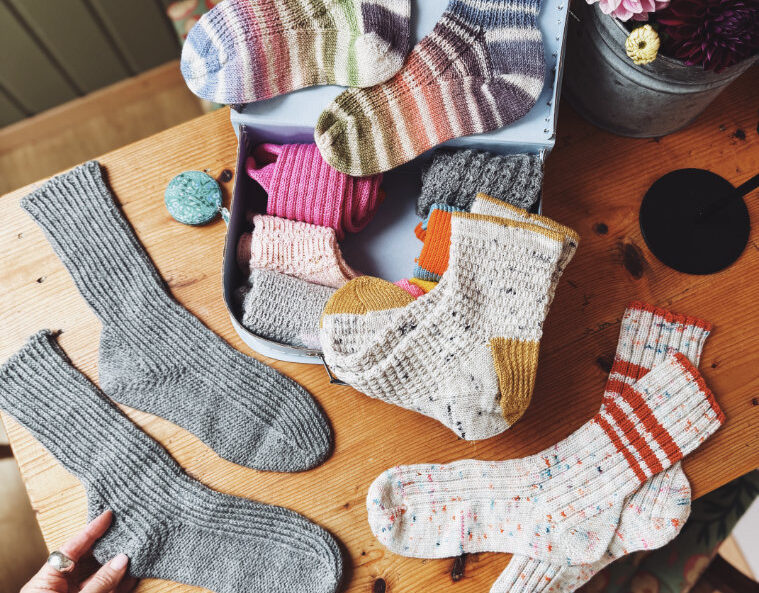 Handgestrickte rosa p. Socken – verschiedene Modelle in Grau, Beige und Bunt, dekorativ auf einem Holztisch arrangiert
