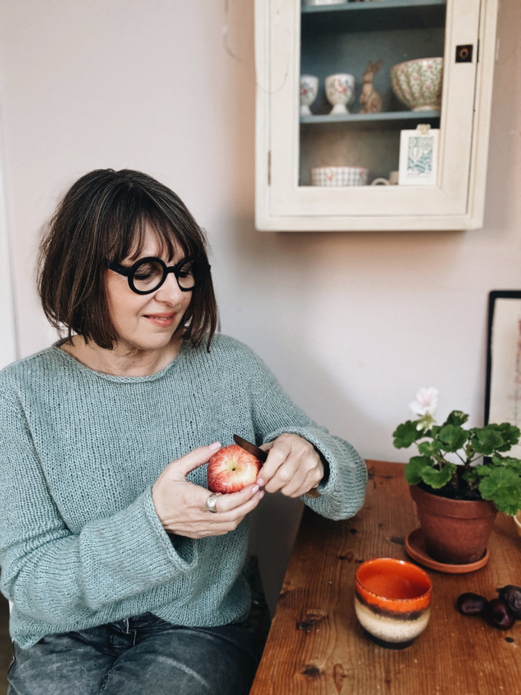 Uukii Sweater in Mint, sitzend am Tisch, Apfel schneidend.