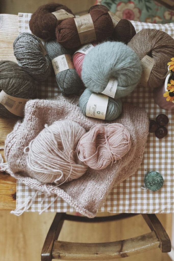 Zusammengelegter Strickpullover in Naturtönen, weiche Strickdecke und Garnknäuel – Stillleben aus dem rosa p. Arbeitsalltag.