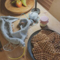 Strickprojekt auf dem Tisch mit Waffeln, Garn und Nadeln – ruhige Szene aus dem Strickalltag im Winter.