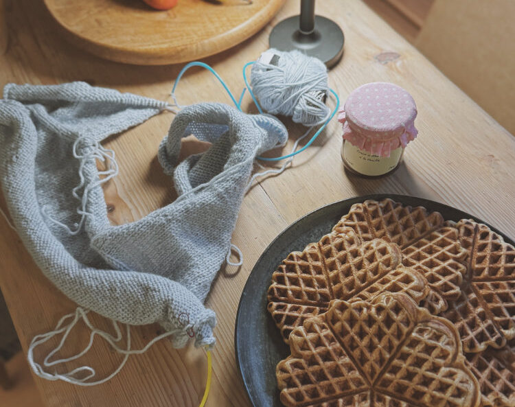 Strickprojekt auf dem Tisch mit Waffeln, Garn und Nadeln – ruhige Szene aus dem Strickalltag im Winter.