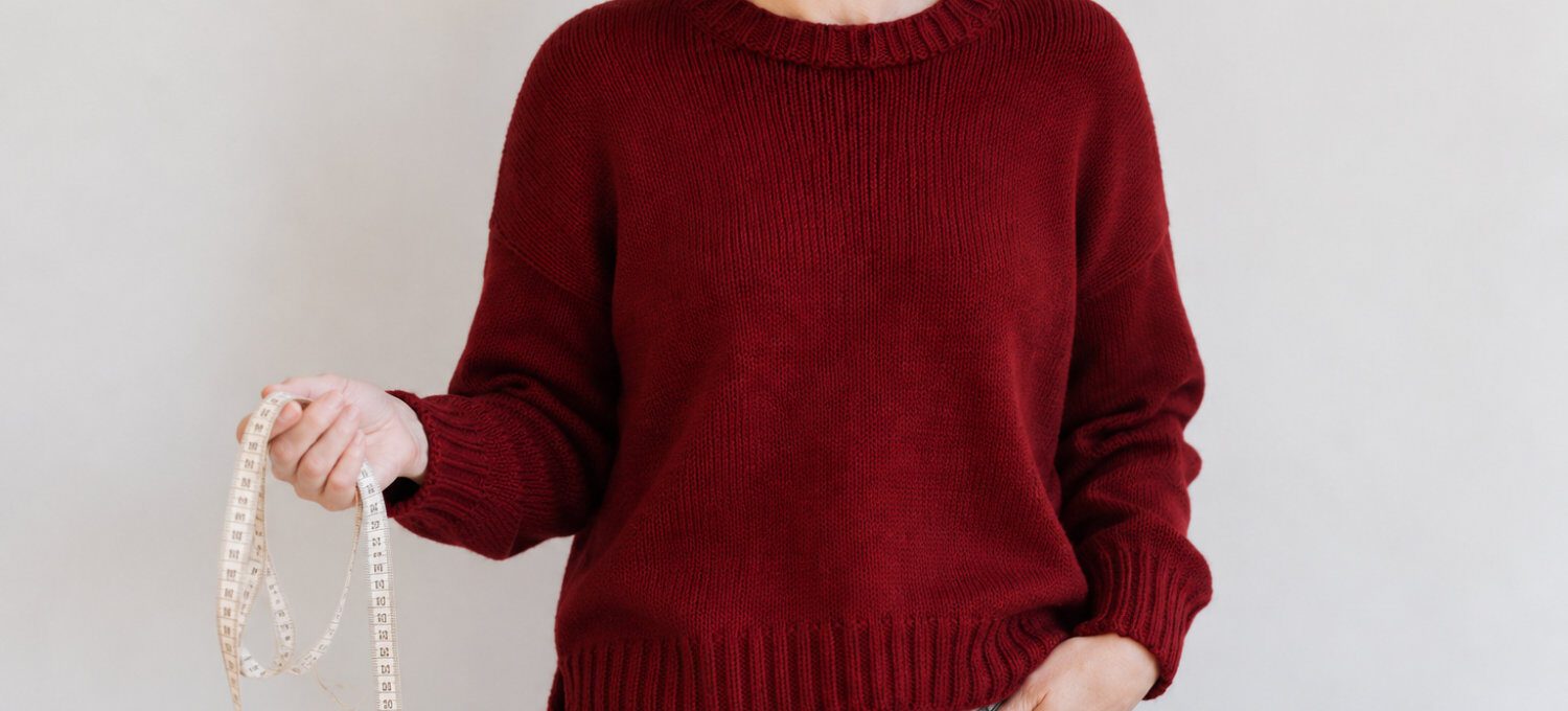 Kaiili Jumper in Dunkelrot, getragen mit Maßband zur Größenwahl einer Strickanleitung.