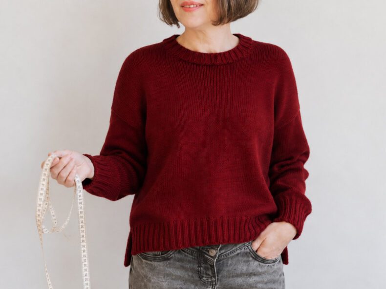 Kaiili Jumper in Dunkelrot, getragen mit Maßband zur Größenwahl einer Strickanleitung.