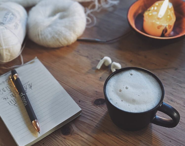 Erikka Vest Projektstimmung – Garn, Notizbuch und Kaffee auf Holztisch.