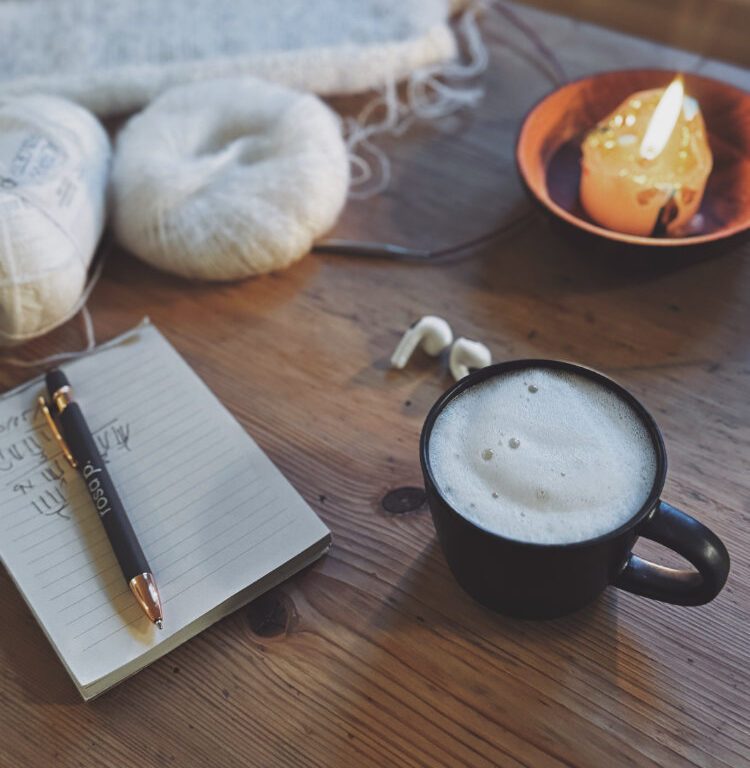 Erikka Vest Projektstimmung – Garn, Notizbuch und Kaffee auf Holztisch.