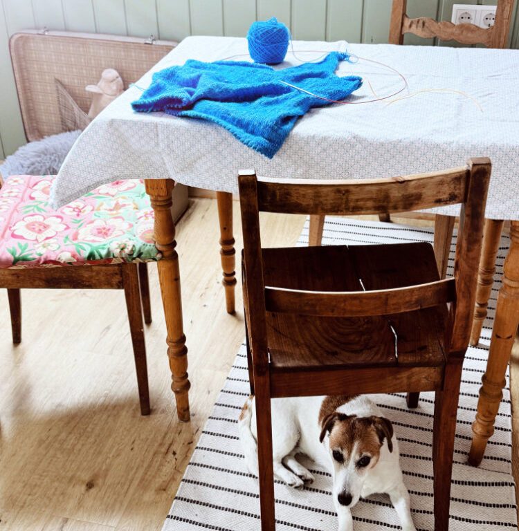 Niine Top aus feinem Sommergarn in kräftigem Blau, als begonnenes Strickprojekt mit Wolle und Rundstricknadel auf einem Holztisch