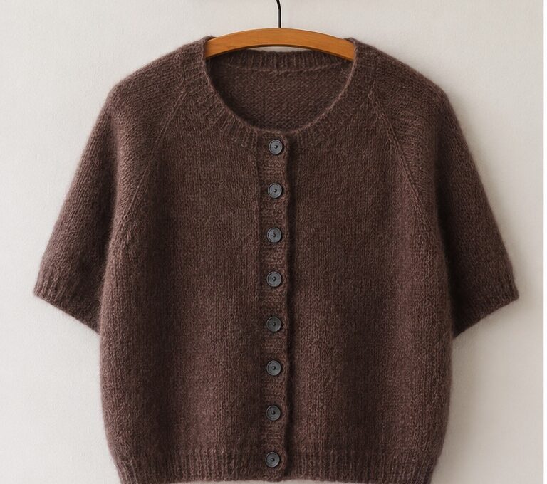 Doorli Cardigan Short Sleeve aus braunem Mohairgarn mit kurzen Ärmeln auf einem Bügel vor heller Wand