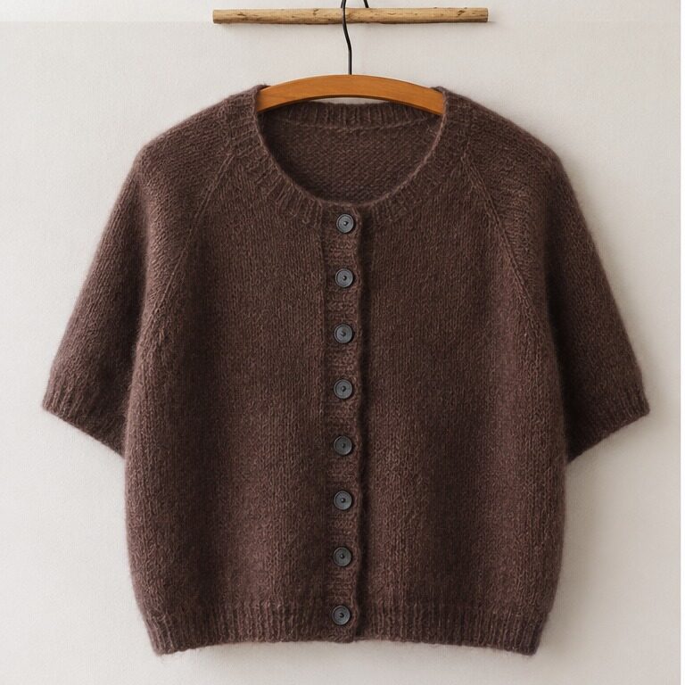 Doorli Cardigan Short Sleeve aus braunem Mohairgarn mit kurzen Ärmeln auf einem Bügel vor heller Wand