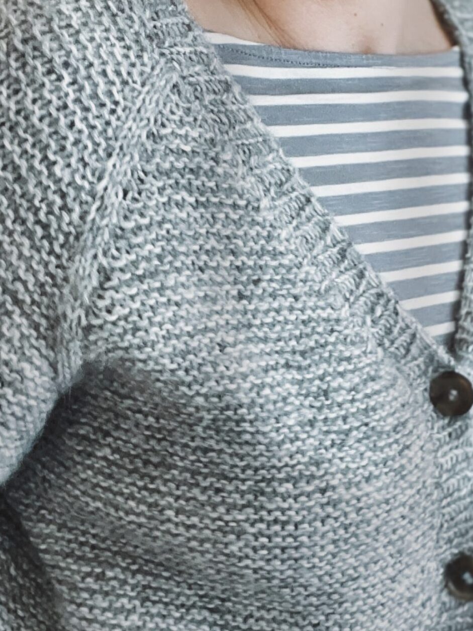 Frau mit verschlossenem Piilo Cardigan – gestrickt von oben in einem Stück mit V-Ausschnitt und Raglanärmeln.