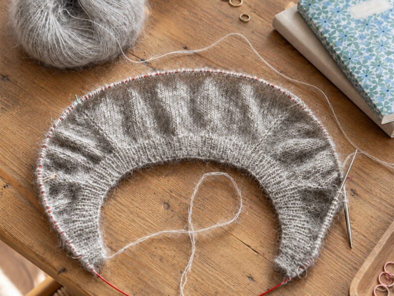 Graues Strickstück mit verkürzten Reihen und sichtbarer Formgebung auf der Rundstricknadel